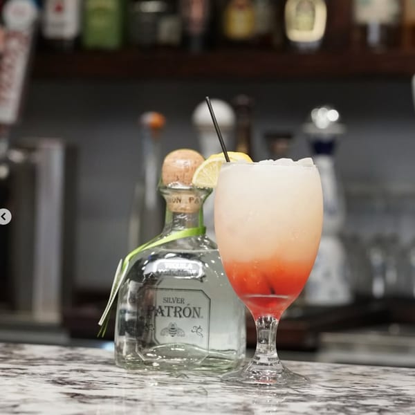 A Kountry Kitchen cocktail with ice, lemon, and a Patron bottle on a marble bar.