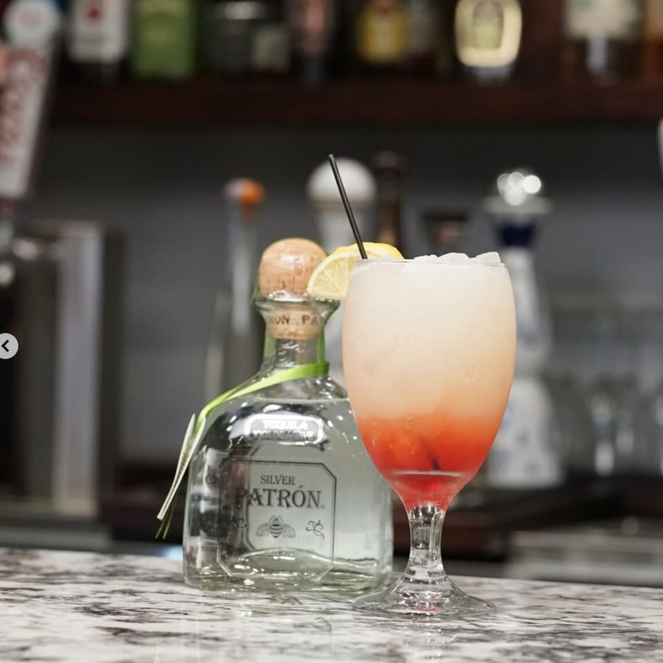 A Kountry Kitchen cocktail with ice, lemon, and a Patron bottle on a marble bar.