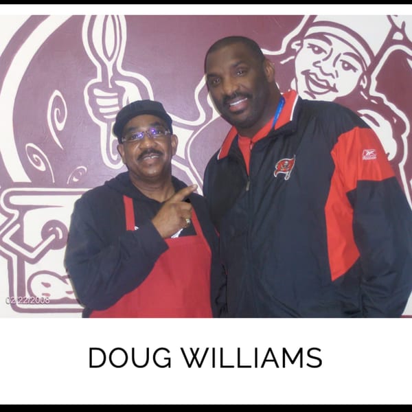 Kountry Kitchen owner in a red apron with Doug Williams, both smiling in front of a mural.