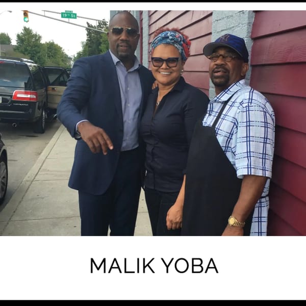 Actor Malik Yoba, a woman, and a man in an apron pose outside Kountry Kitchen soul food restaurant.