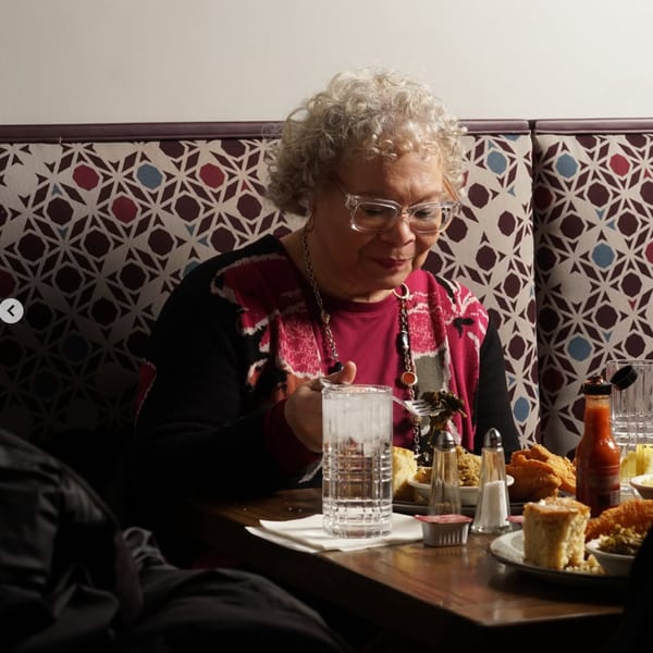 A woman with curly gray hair and glasses eats soul food at Kountry Kitchen.