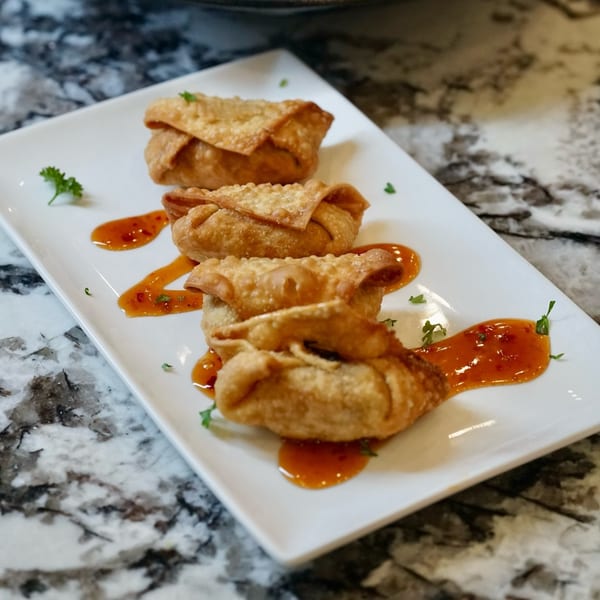 Four golden-fried wontons with sweet chili sauce and parsley on a white rectangular plate.
