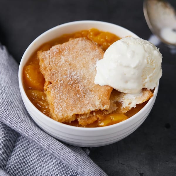 A white bowl of Kountry Kitchen's peach cobbler with a scoop of vanilla ice cream.