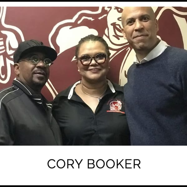 Kountry Kitchen owners pose with Cory Booker in front of a red wall with a white logo.