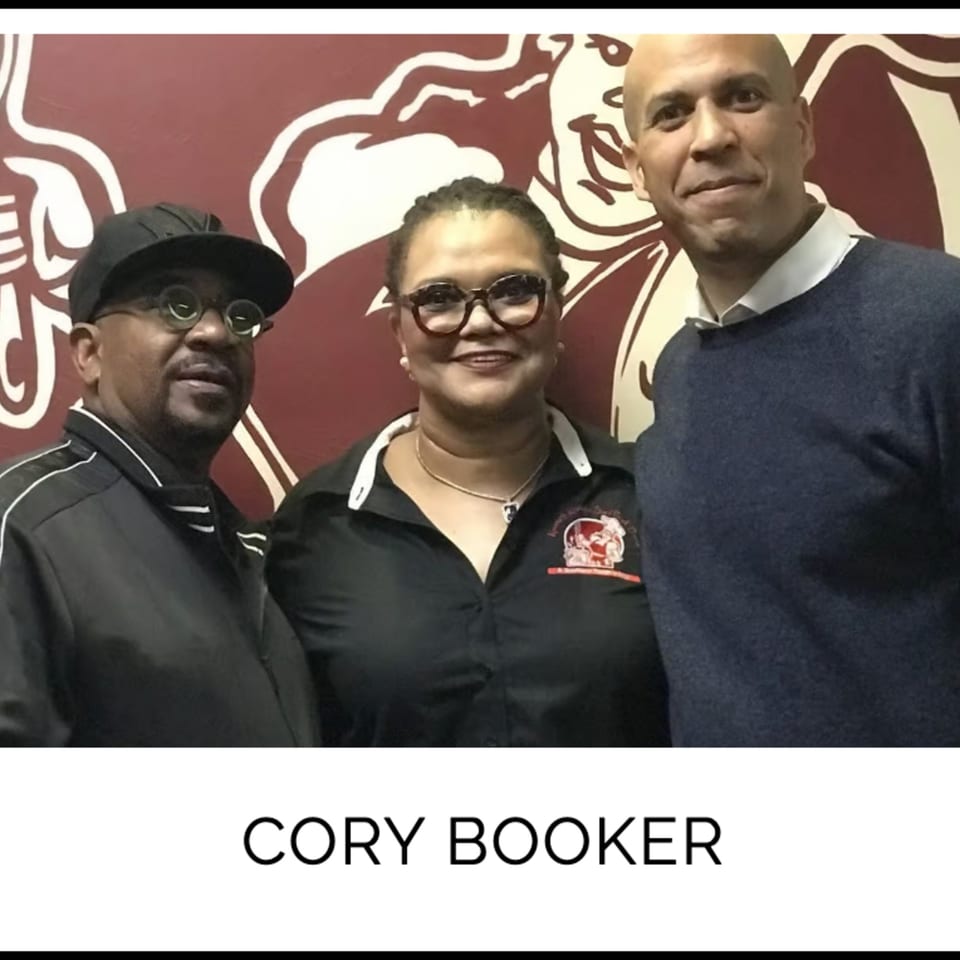 Kountry Kitchen owners pose with Cory Booker in front of a red wall with a white logo.