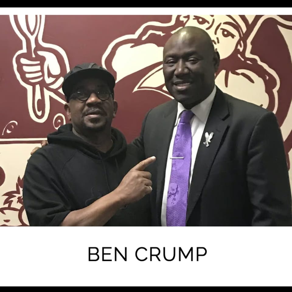 Ben Crump and another man smiling in front of a Kountry Kitchen wall mural.