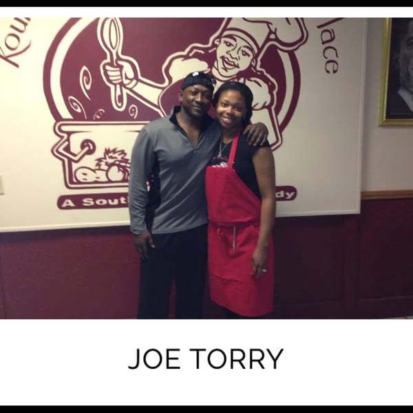 Joe Torry and a woman in a red apron pose in front of Kountry Kitchen's chef logo.