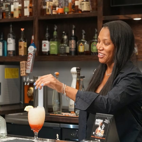 A smiling bartender at Kountry Kitchen serves a colorful cocktail at a well-stocked bar.