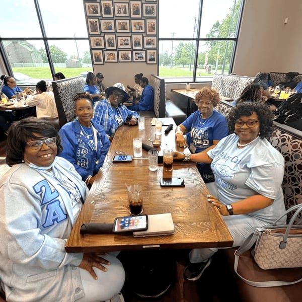 Group of women in blue and white shirts smiling at a long wooden table in Kountry Kitchen.