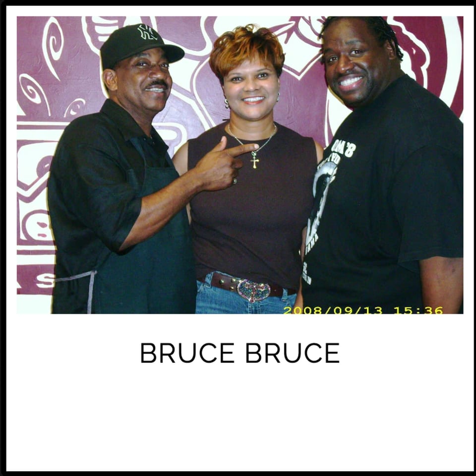 Three smiling people, two men and one woman, posing together in front of a purple and white patterned wall.