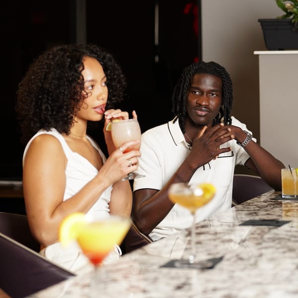 A couple enjoying cocktails at a bar, with the woman sipping from a straw.
