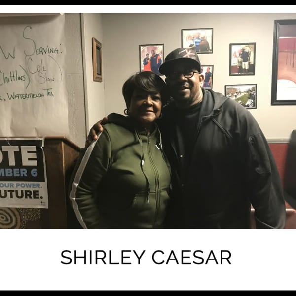 Shirley Caesar and a man posing together in Kountry Kitchen, with framed photos on the wall.
