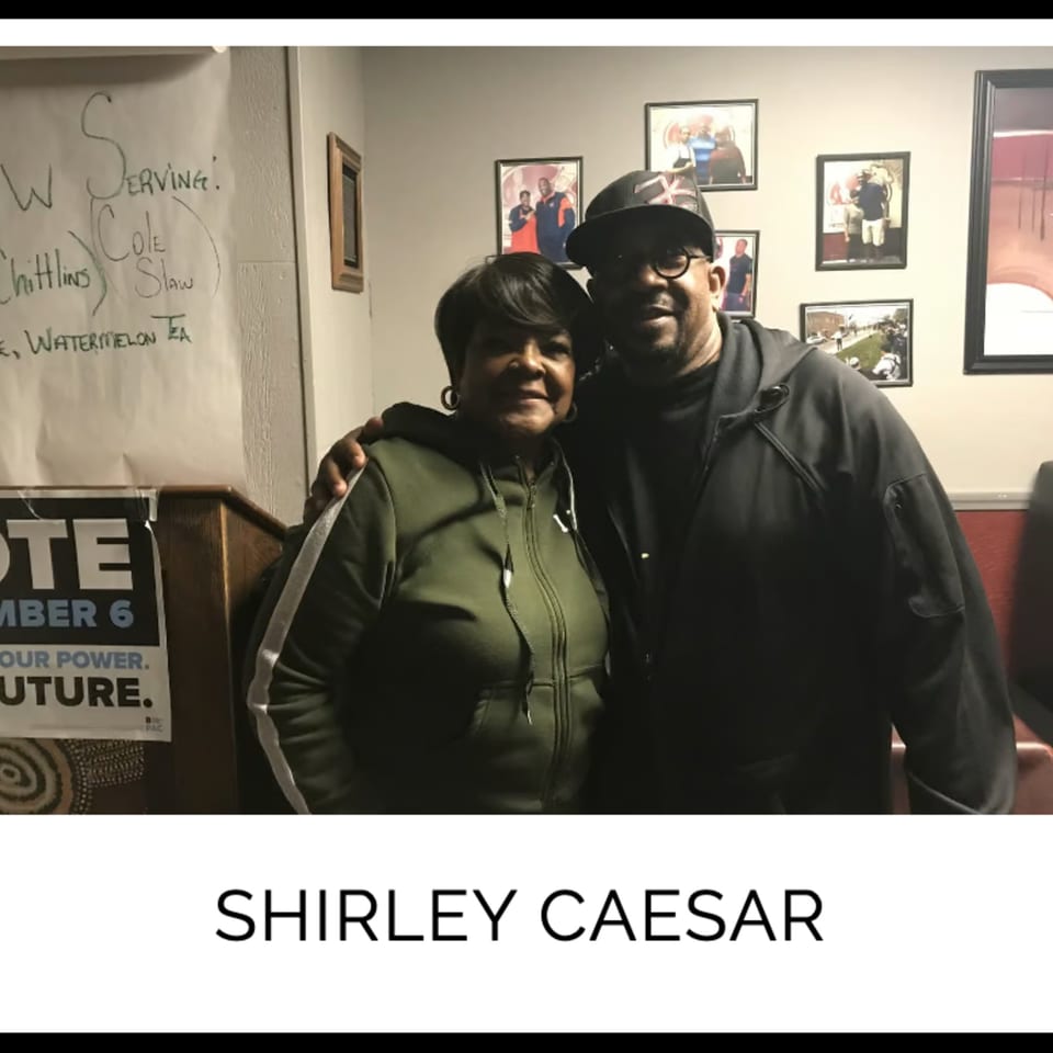 Shirley Caesar and a man posing together in Kountry Kitchen, with framed photos on the wall.