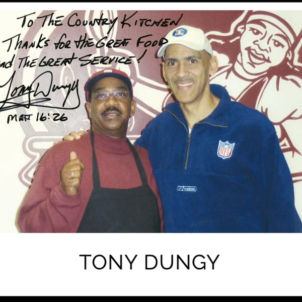 Tony Dungy and a Kountry Kitchen employee smiling, with a signed message on the wall.
