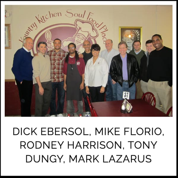 A group of men, including Dick Ebersol and Tony Dungy, pose in front of the Kountry Kitchen logo.