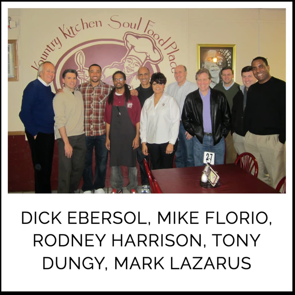 A group of men, including Dick Ebersol and Tony Dungy, pose in front of the Kountry Kitchen logo.