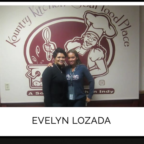 Two women smiling, posing in front of the Kountry Kitchen soul food restaurant logo.