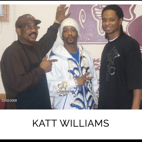 Katt Williams posing with two men, one in a brown shirt and the other in a black shirt.