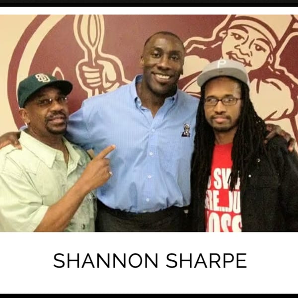 Shannon Sharpe smiling with two men, one pointing at him, in front of a Kountry Kitchen logo.