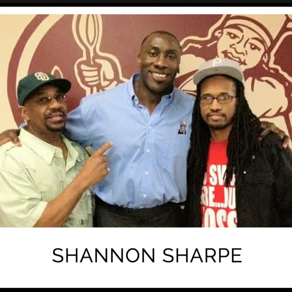 Shannon Sharpe smiling with two men, one pointing at him, in front of a Kountry Kitchen logo.