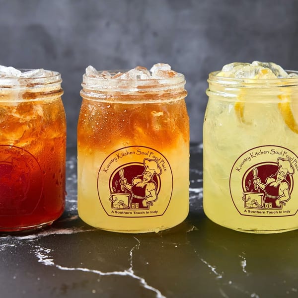 Three Kountry Kitchen mason jars with iced tea and lemonade on a dark, marbled surface.