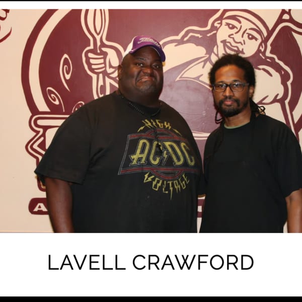 Lavell Crawford and another man pose in front of a Kountry Kitchen mural.