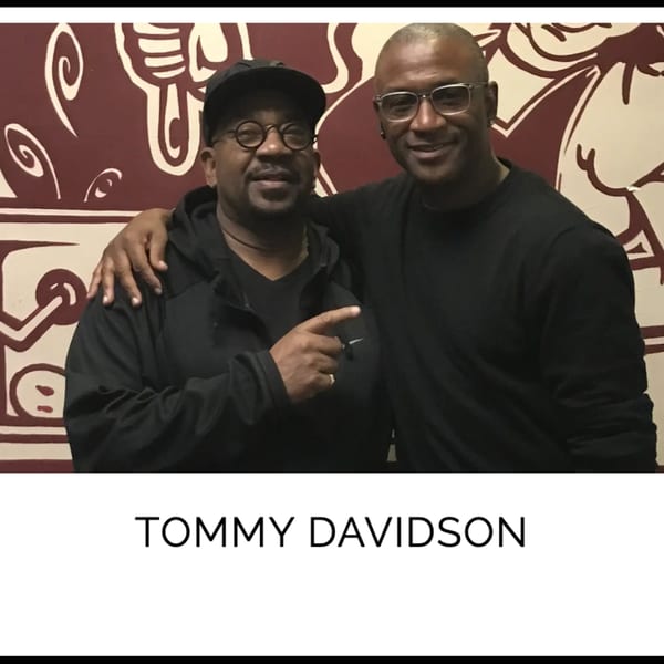 Tommy Davidson and another man smiling, with the man on the left pointing forward.