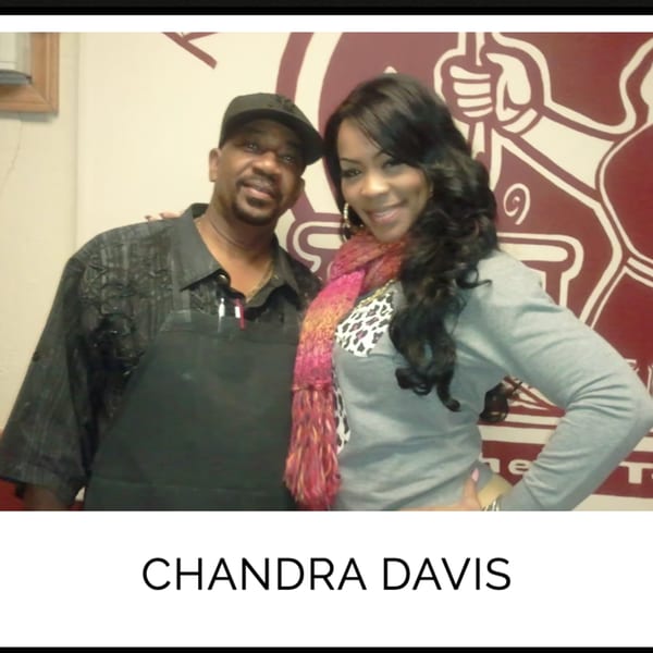 Chandra Davis and a man smiling together in front of a Kountry Kitchen wall mural.