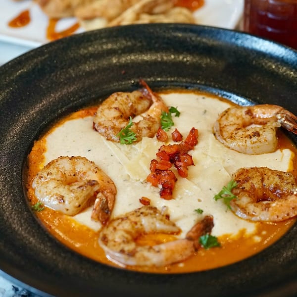 Kountry Kitchen's shrimp and grits, garnished with bacon and parsley, in a black bowl.
