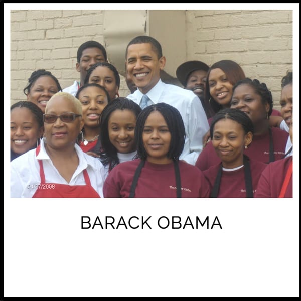 Barack Obama smiling with a group of Kountry Kitchen staff wearing aprons.