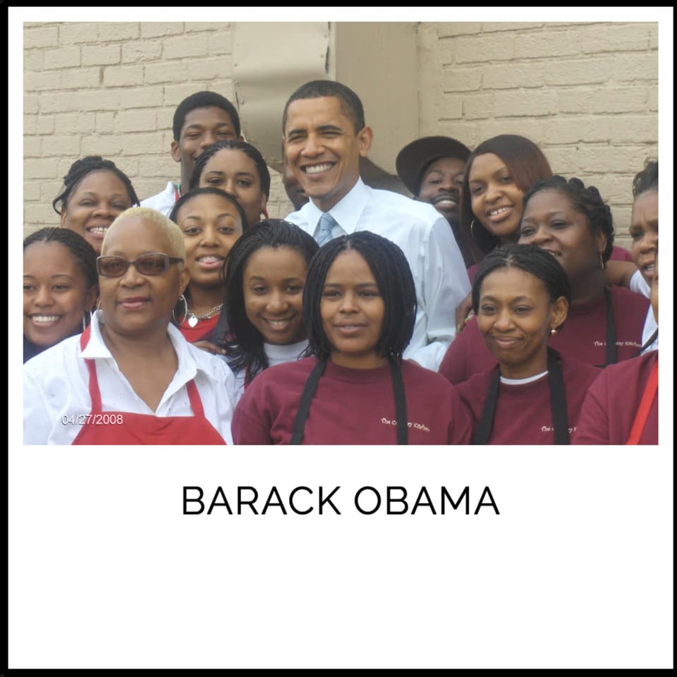Barack Obama smiling with a group of Kountry Kitchen staff wearing aprons.
