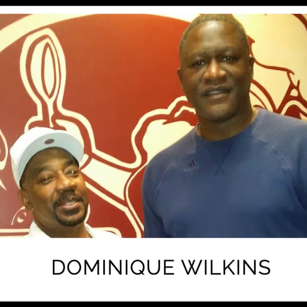 Dominique Wilkins and another man smiling in front of a Kountry Kitchen wall mural.